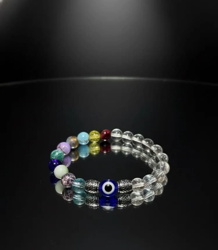 Evil Eye Chakra Guardian Bracelet with Clear Quartz beads and metal spacers on a black reflective surface.