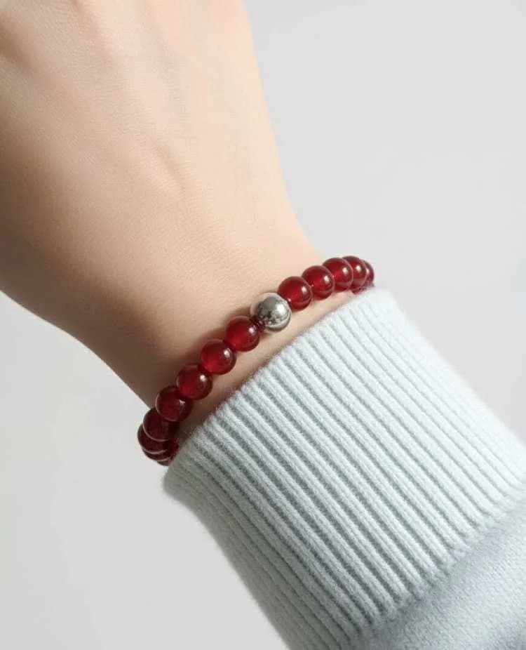 A person wearing a light blue sweater wears a translucent red Carnelian beaded bracelet with a single silver spacer on their wrist.