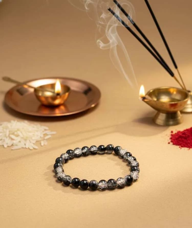 A Black Tourmaline and Clear Quartz beaded bracelet surrounded by spiritual items like burning incense, kumkum, rice, and a lit diya (oil lamp).