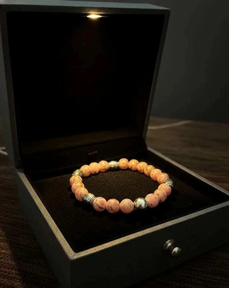 A light peach/coral-pink patterned Jasper beaded bracelet with silver patterned spacers, displayed in an open black jewelry box with interior light.