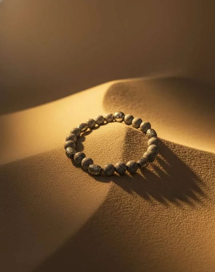 A grey and white marbled Agate beaded bracelet with silver ornate spacers, displayed on sand dunes under dramatic shadows and sunlight.