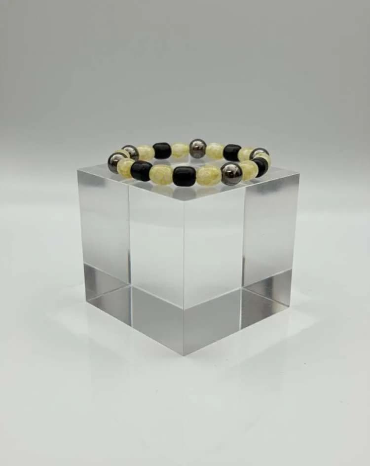 A bracelet with alternating yellow Quartz and black Onyx beads, interspersed with metallic silver spacers, displayed on a clear acrylic block.