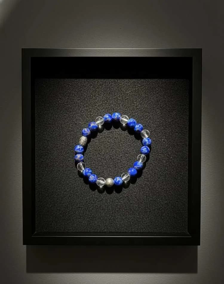 A bracelet with alternating blue Lapis Lazuli and clear Quartz beaded, resting inside a black frame/display box.