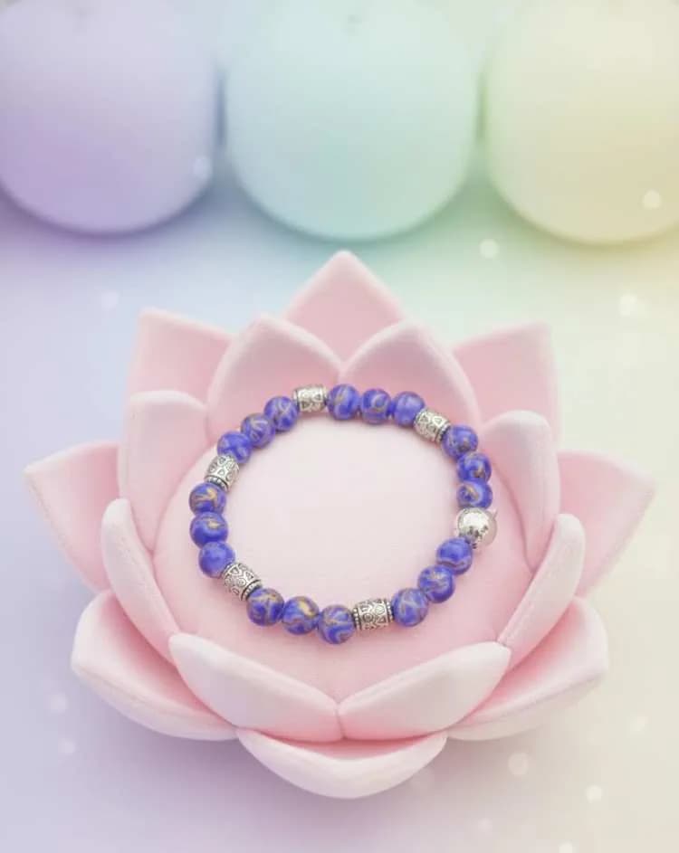 A vibrant blue patterned Imperial Jasper beaded bracelet with silver spacers, resting on a pink lotus flower cushion in soft, pastel lighting.