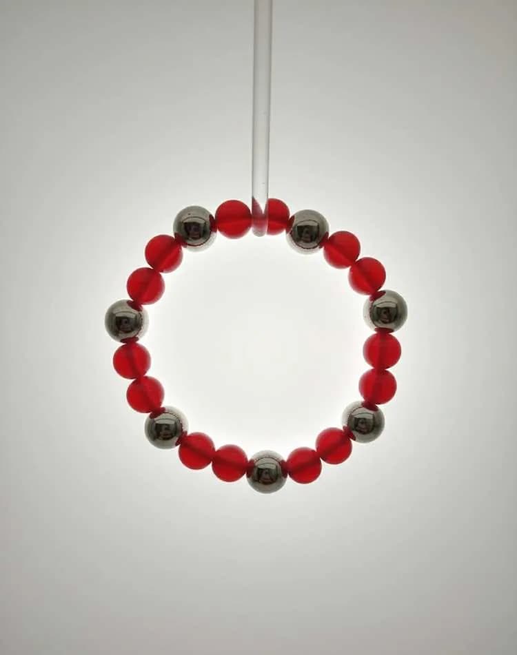 A bracelet with alternating translucent red Agate beads and metallic silver Hematite beads, illuminated from behind on a white background.